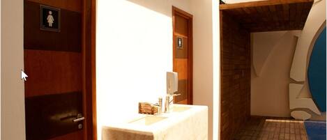 A bathroom with a wooden door, a sink with a mirror, and a shower area with a blue tiled wall.