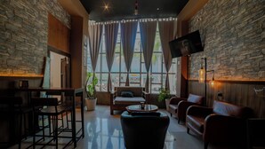 A spacious lounge area with a stone wall, comfortable seating, a flat-screen TV, and large windows.