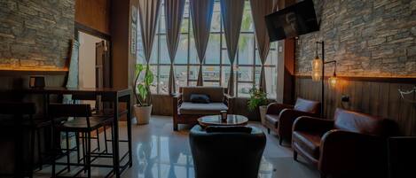 A spacious lounge area with a stone wall, comfortable seating, a flat-screen TV, and large windows.