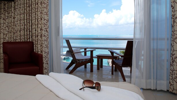 A hotel room with a large bed, a red armchair, and a view of the ocean through sheer curtains.