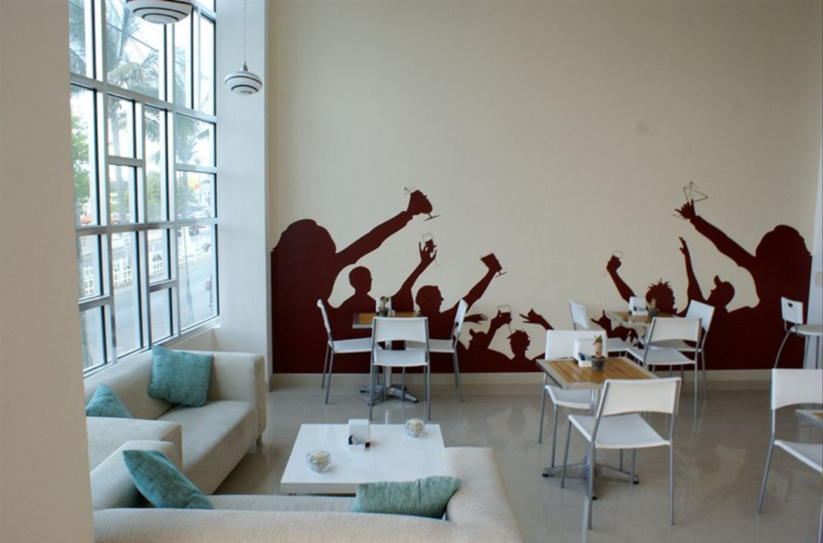 Et moderne værelse med et stort vindue, en sofa, et spisebord med stole og et mural med silhuetfigurer.