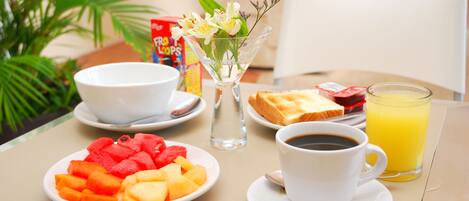 Una mesa de desayuno con un bol blanco, un vaso de jugo de naranja, una taza de café y platos de fruta.