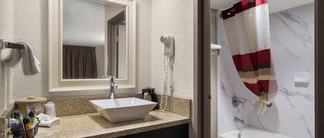 A bathroom with a white sink, a mirror, a hairdryer, and a shower curtain.