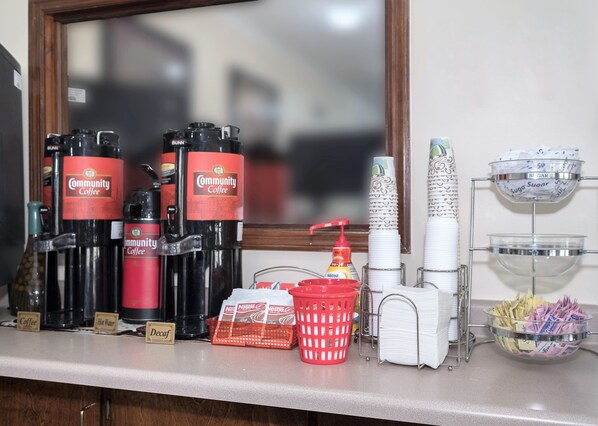 A coffee station with dispensers, a red basket, and a dispenser of napkins.