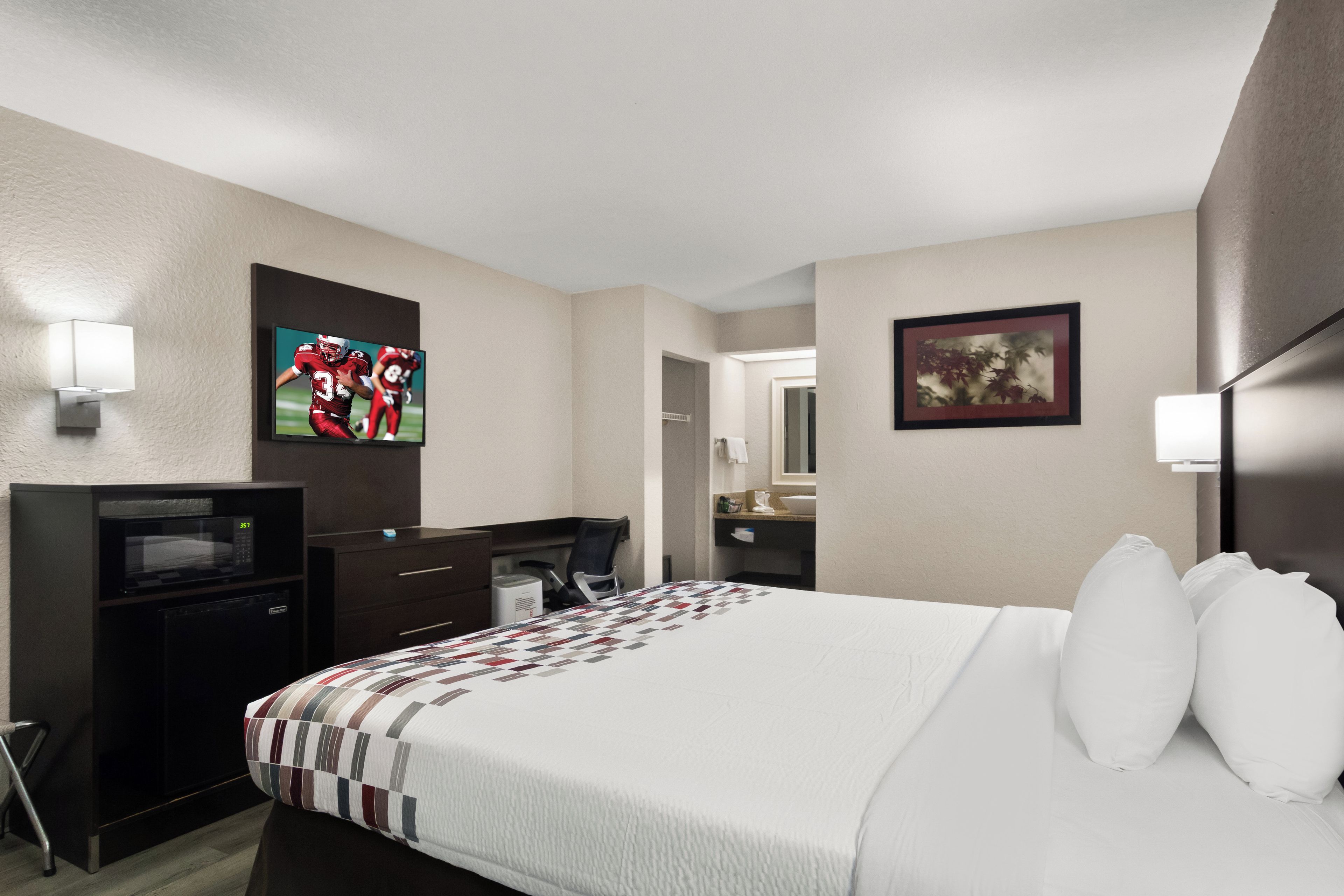 Une chambre d’hôtel équipée d’un lit, d’un bureau, d’une télévision et ornée d’œuvres d’art aux murs.