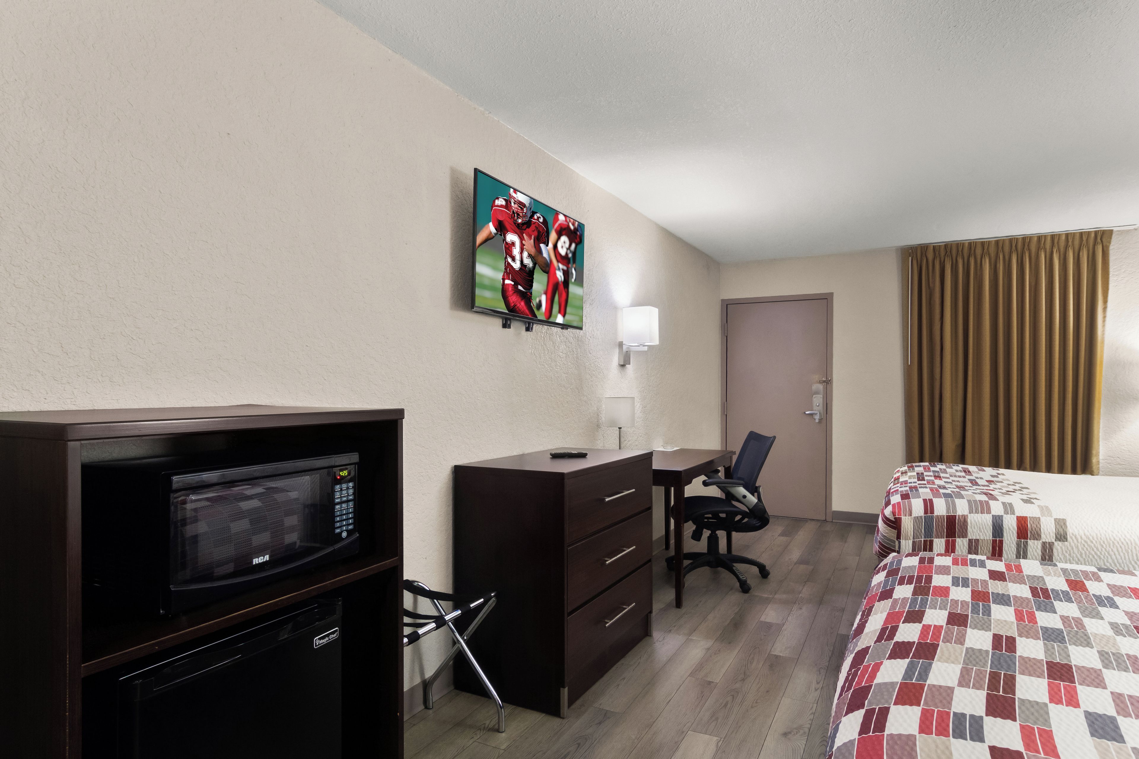 Une chambre d’hôtel avec un lit, un bureau, une chaise, une télévision, un four à micro-ondes et un tableau au mur.