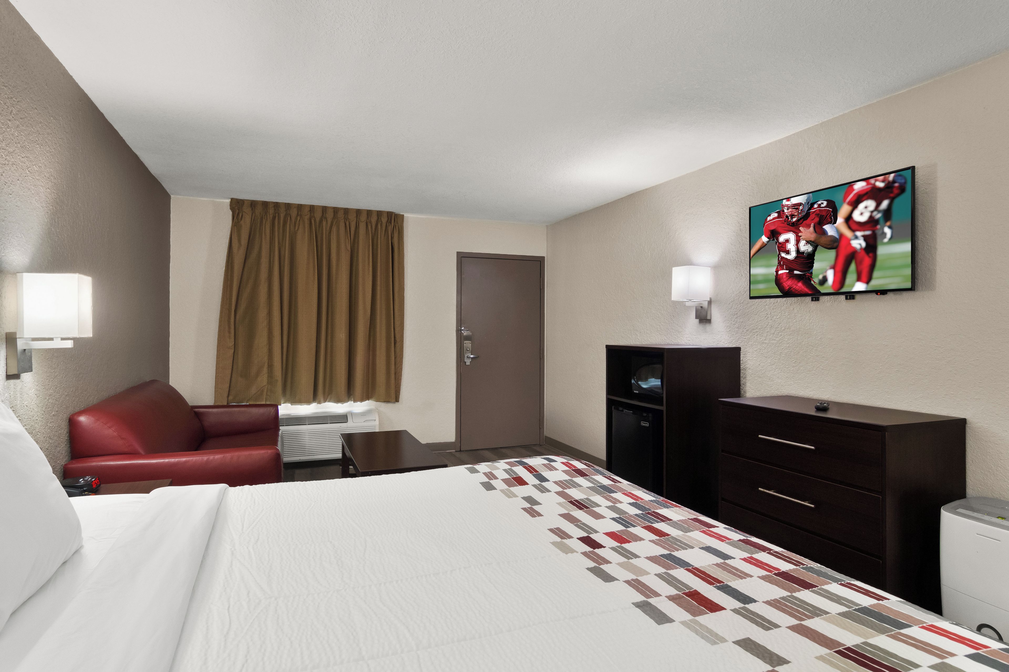 Ein Hotelzimmer mit einem Bett, einem roten Sessel, einem Schreibtisch, einem Fernseher und einem Kleiderschrank.