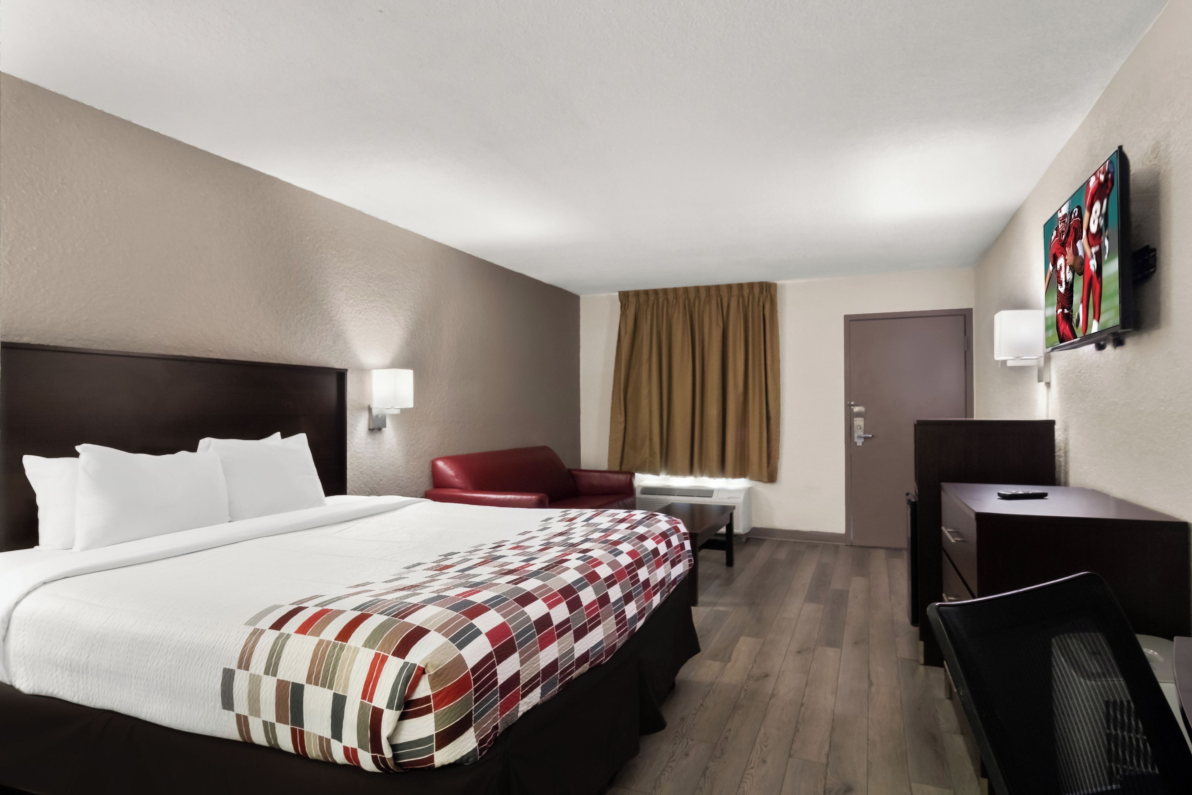 Una habitación de hotel con una cama grande, un escritorio, una silla, un televisor y una puerta.