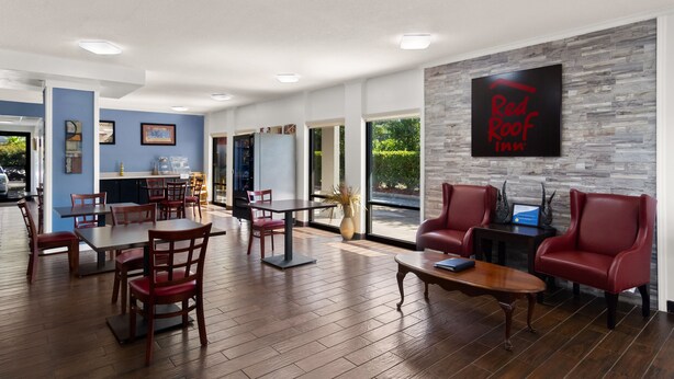 A modern hotel lobby with wooden flooring, red leather seating, and a Red Roof Inn sign on the wall.