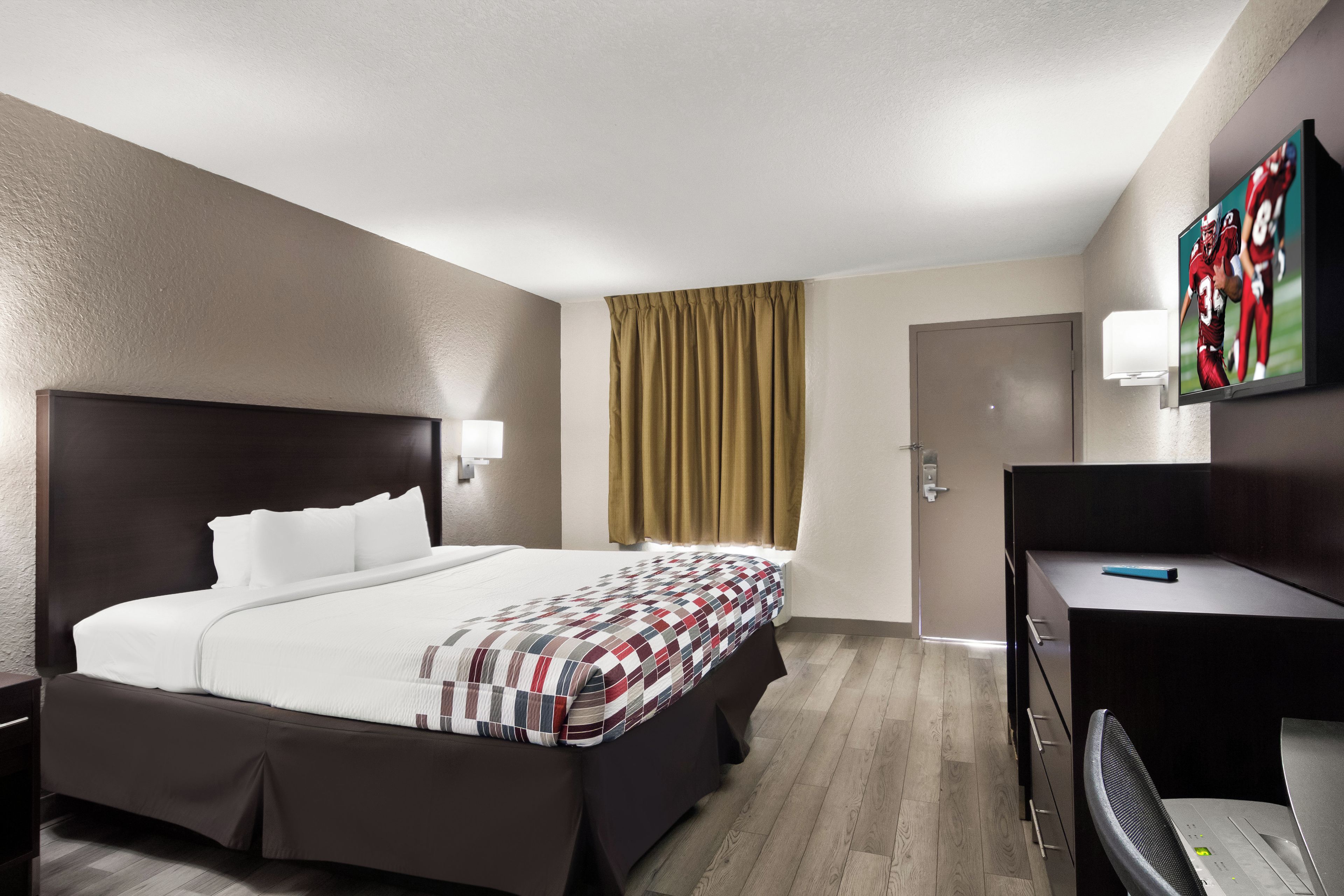 Ein Hotelzimmer mit einem großen Bett, einem Schreibtisch, einem Sessel, einem Fernseher und einer Tür.