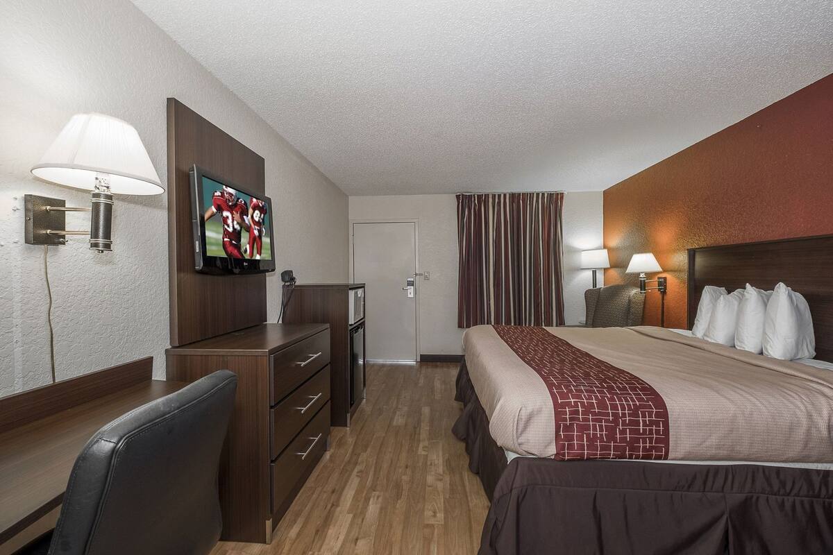 A hotel room with a bed, desk, chair, TV, and curtains.