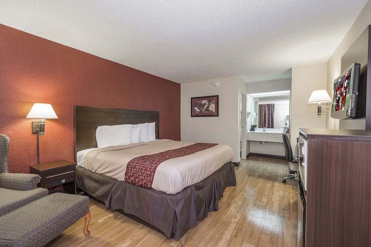 A hotel room with a bed, bedside lamp, chair, desk, and a mirror.