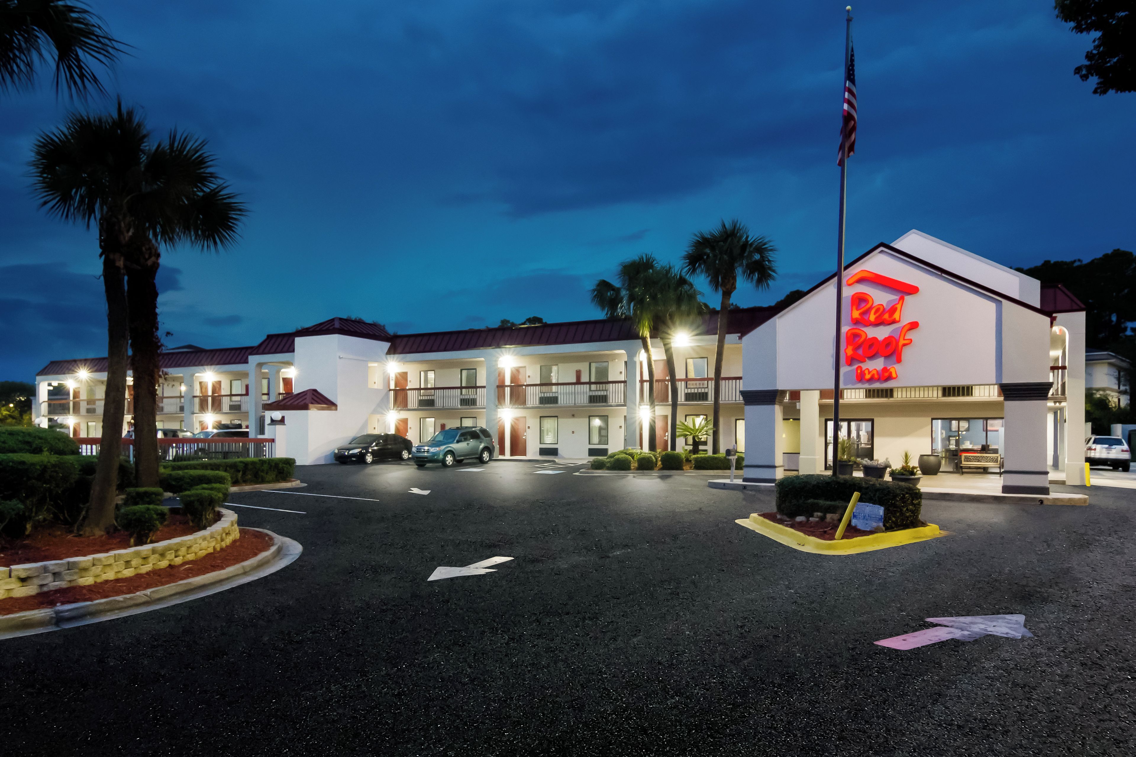 Un hotel Red Roof Inn con estacionamiento, palmeras y cielo despejado.