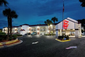 A Red Roof Inn with a parking lot, palm trees, and a clear sky.
