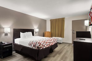 A hotel room with a large bed, bedside tables, a chair, a desk, and a television.
