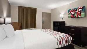 A hotel room with a bed, a TV on the wall, a desk, and a chair.