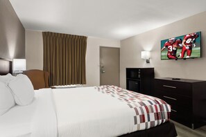 A hotel room with a bed, a TV on the wall, a desk, and a chair.