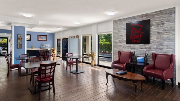 A hotel lobby with a Red Roof Inn sign, wooden tables and chairs, and a stone accent wall.