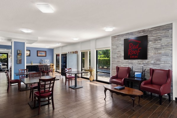 A hotel lobby with a Red Roof Inn sign, wooden tables and chairs, and a stone accent wall.