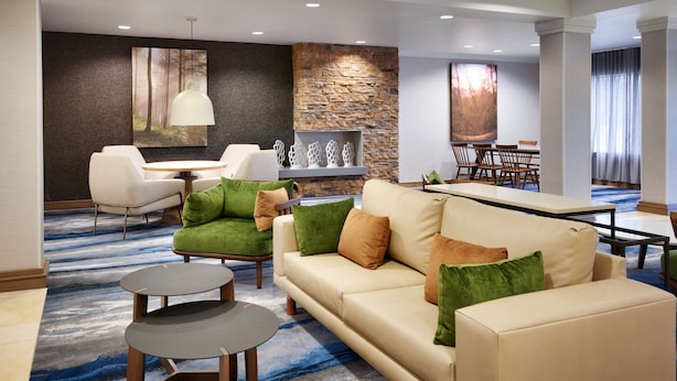 A modern hotel lobby with a beige sofa, green armchairs, a round table, and a stone accent wall. - Fairfield Inn & Suites by Marriott Albany (Albany)