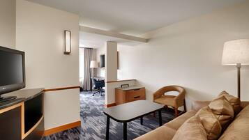 A hotel room with a flat-screen TV, a sofa, a coffee table, a desk, and a chair.