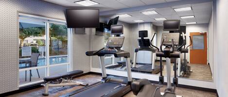A modern gym with treadmills, elliptical machines, and a pool view.