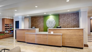 A reception area with a wooden reception desk, a green accent wall, and a patterned wall behind the desk. - Fairfield Inn & Suites by Marriott Albany (Albany)