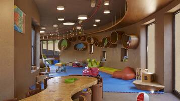 Een kinderspeelruimte met een gebogen houten tafel, kleurrijke speelconstructies en een groot raam dat voor natuurlijk licht zorgt.