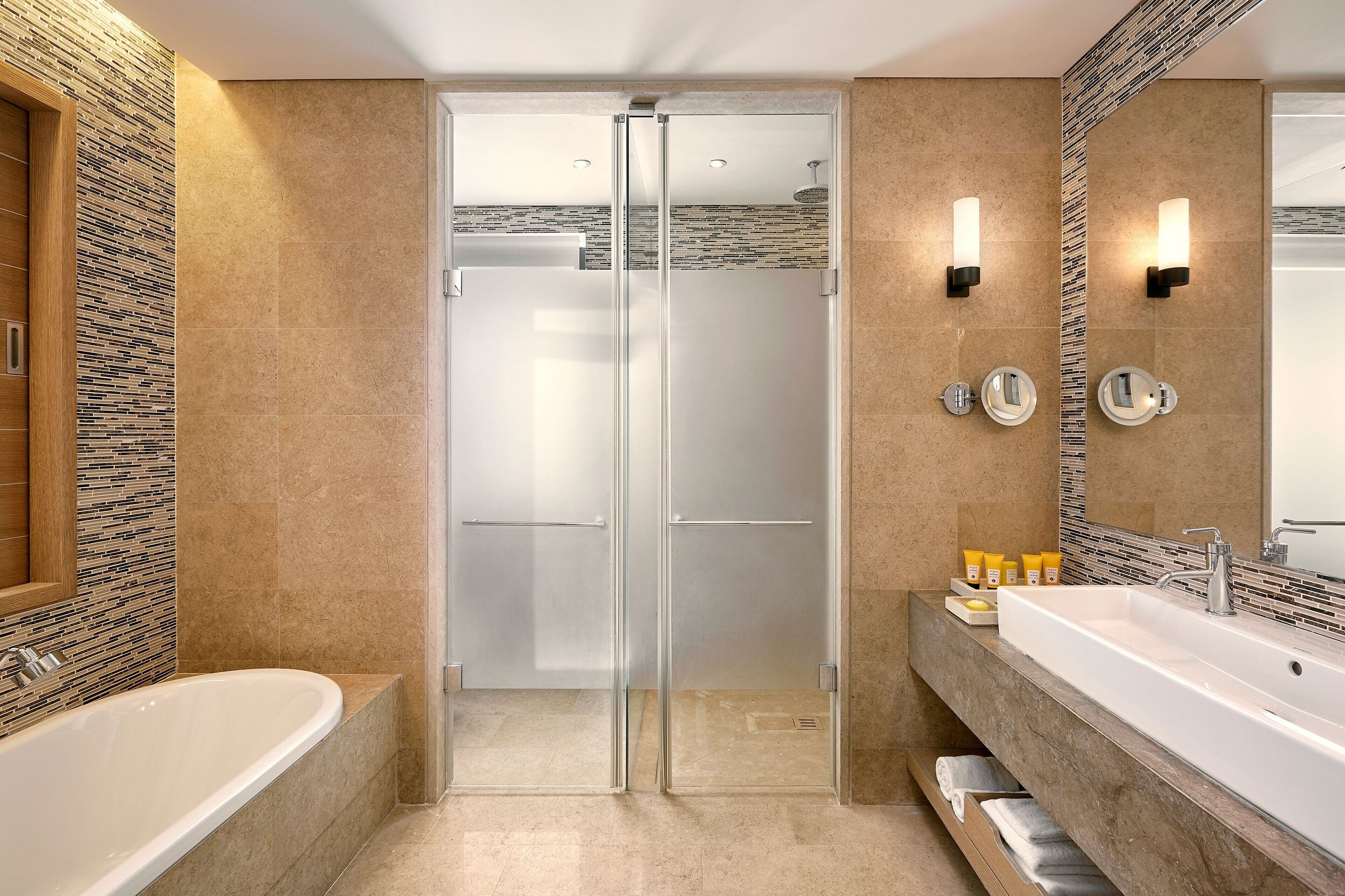 Un baño moderno con ducha de mampara de vidrio, un lavamanos grande y un espejo con apliques de pared.