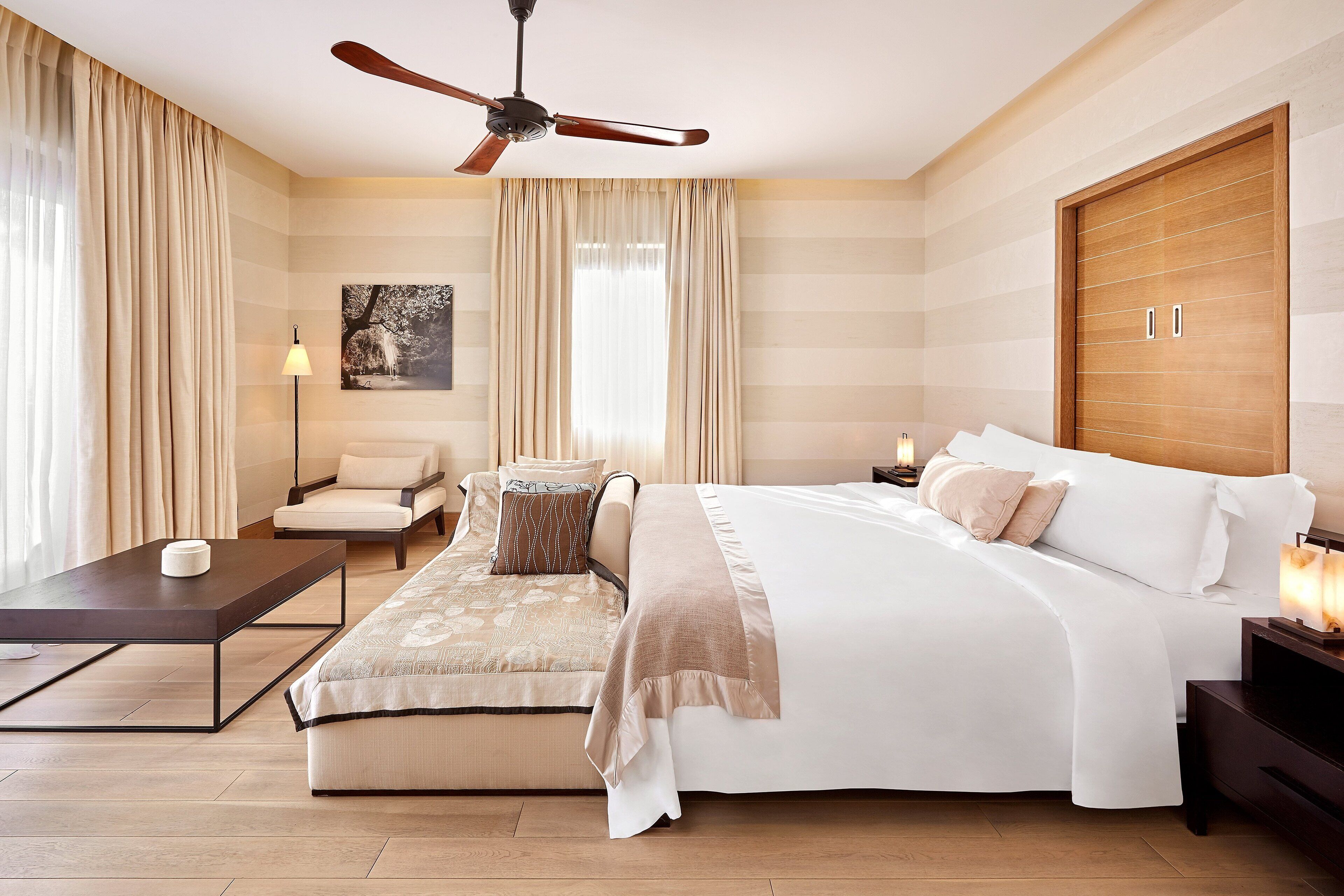 Una habitación de hotel con una cama, un sofá, una mesa de centro, una lámpara y un ventilador de techo.