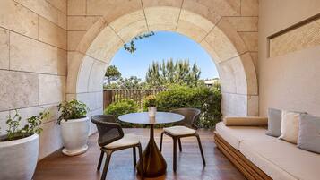 A sunlit patio with a round table and chairs, a cushioned sofa, and potted plants.