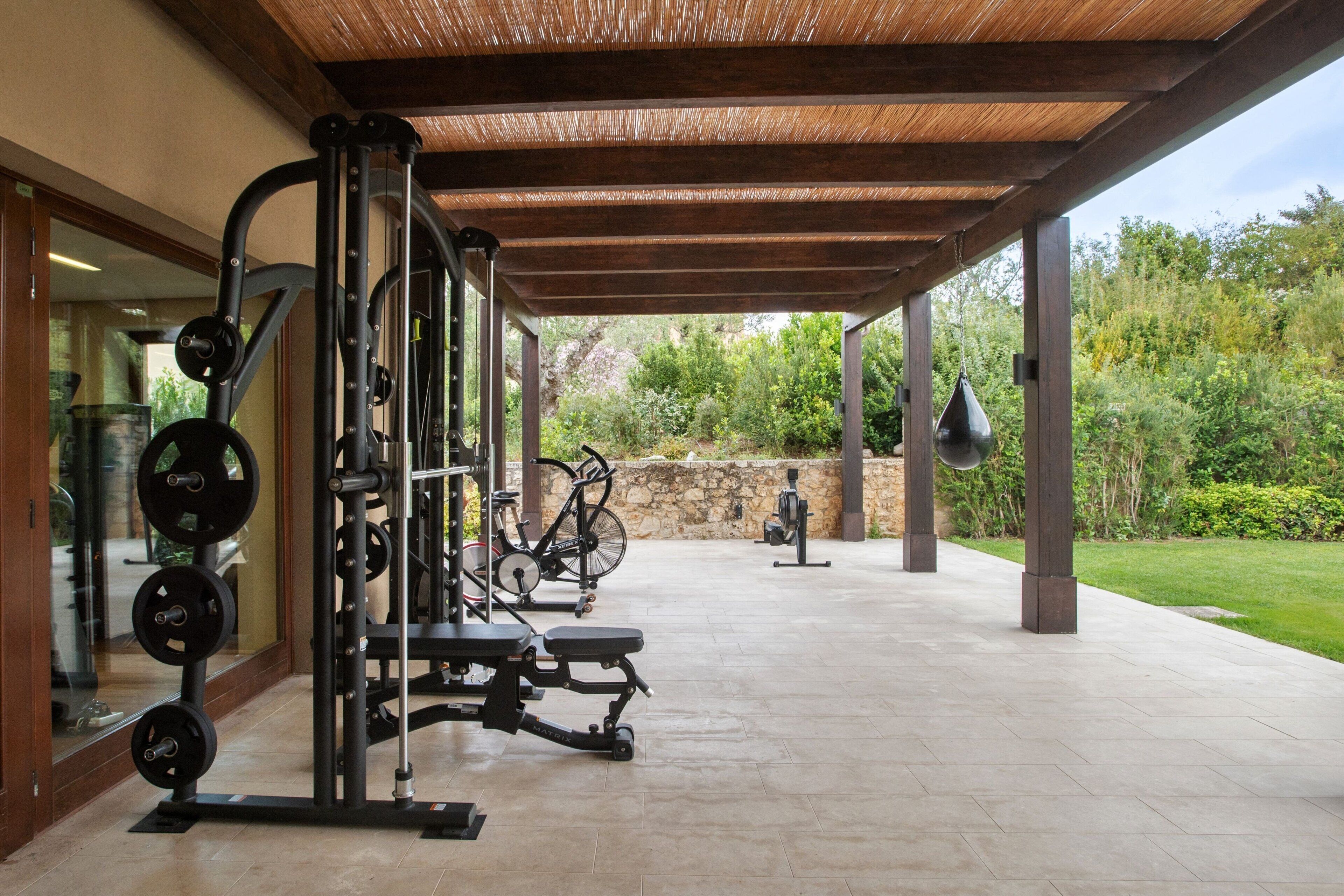 An outdoor gym with exercise equipment, a stone wall, and a grassy area.