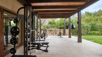 An outdoor gym with exercise equipment, a stone wall, and a grassy area.