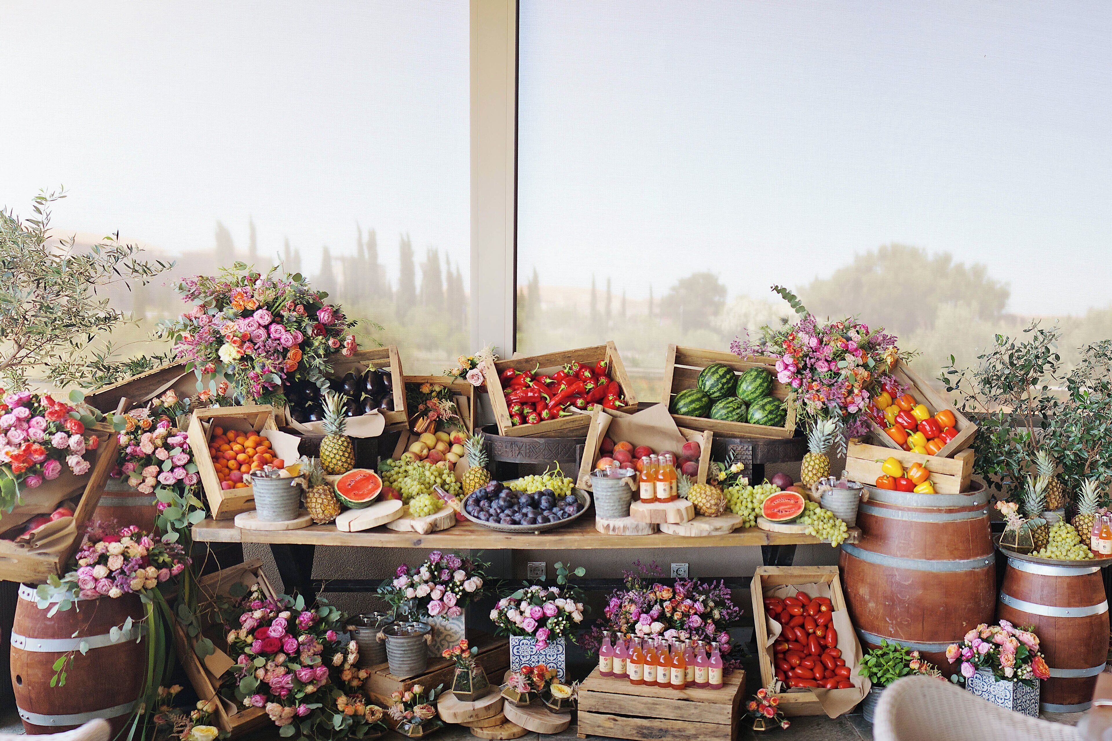 A variety of fruits and flowers displayed on wooden crates and barrels, with a large window in the background.