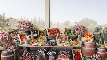A variety of fruits and flowers displayed on wooden crates and barrels, with a large window in the background.