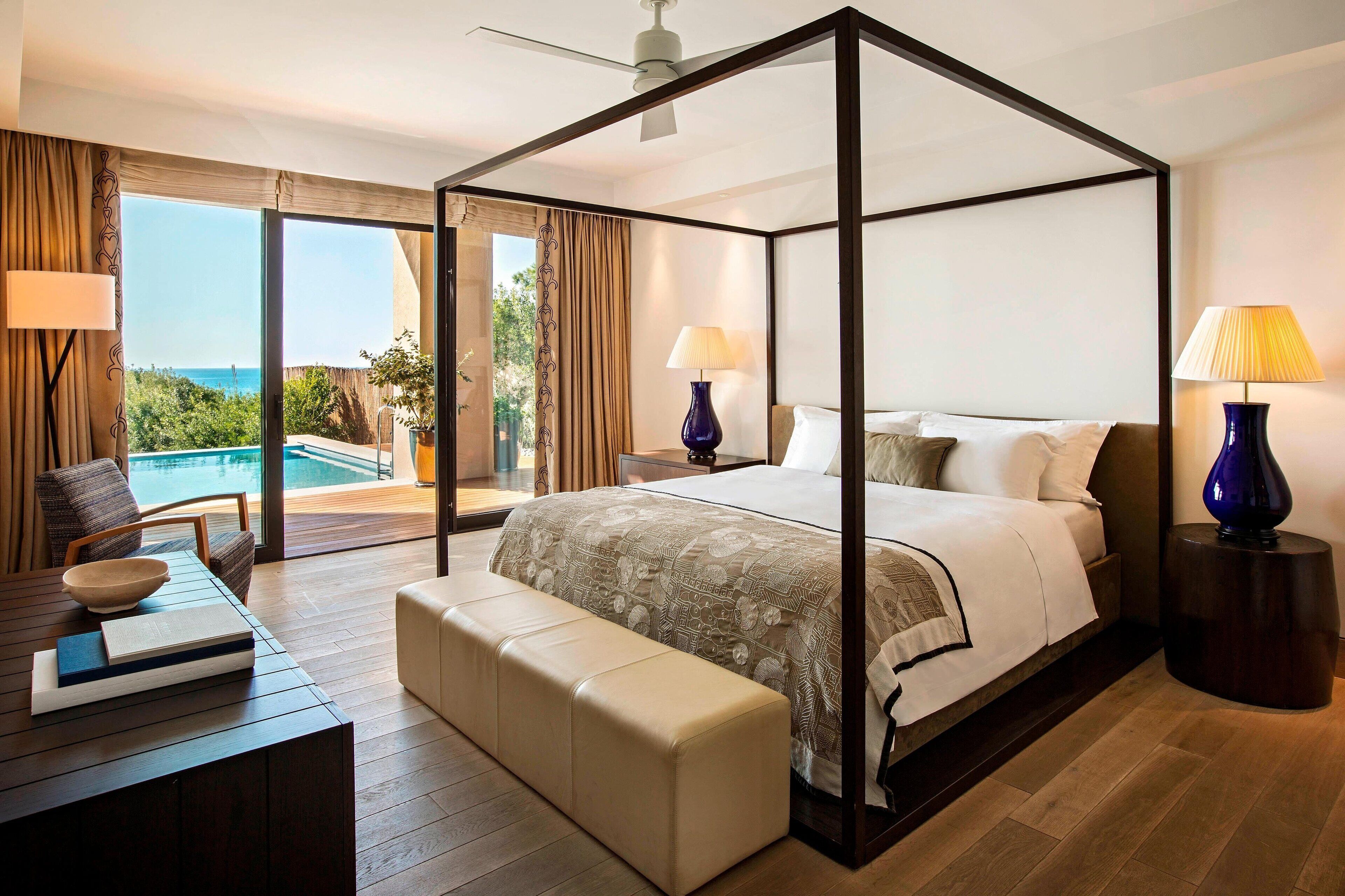 Una cama con dosel y vistas al océano, una piscina y un balcón.