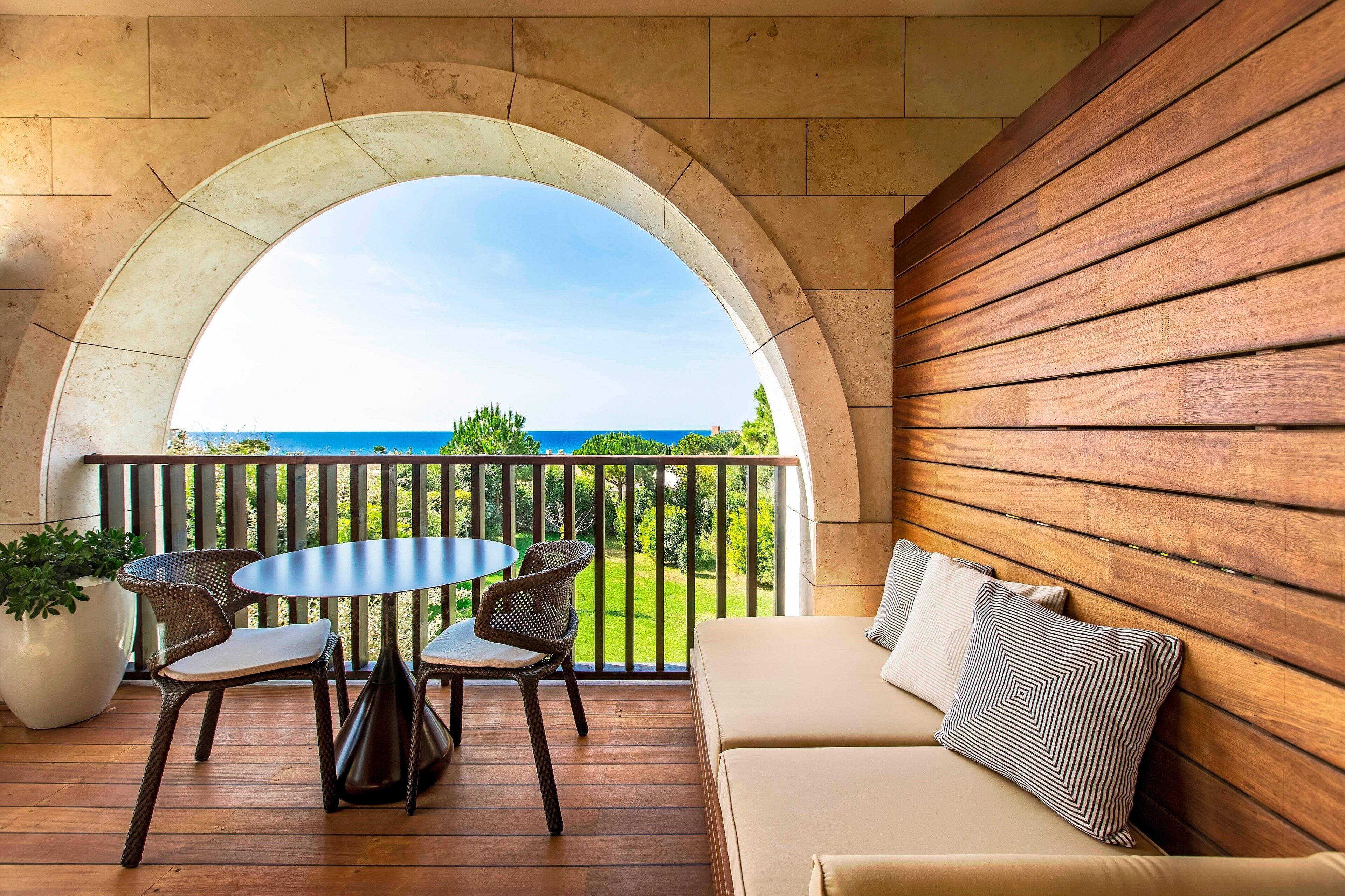 Ein Balkon mit Holztisch und Stühlen, einer Couch und Blick aufs Meer.