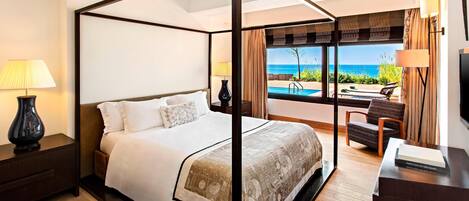 Un lit à baldaquin avec vue sur la mer, un bureau avec une chaise et un téléviseur posé sur un meuble.