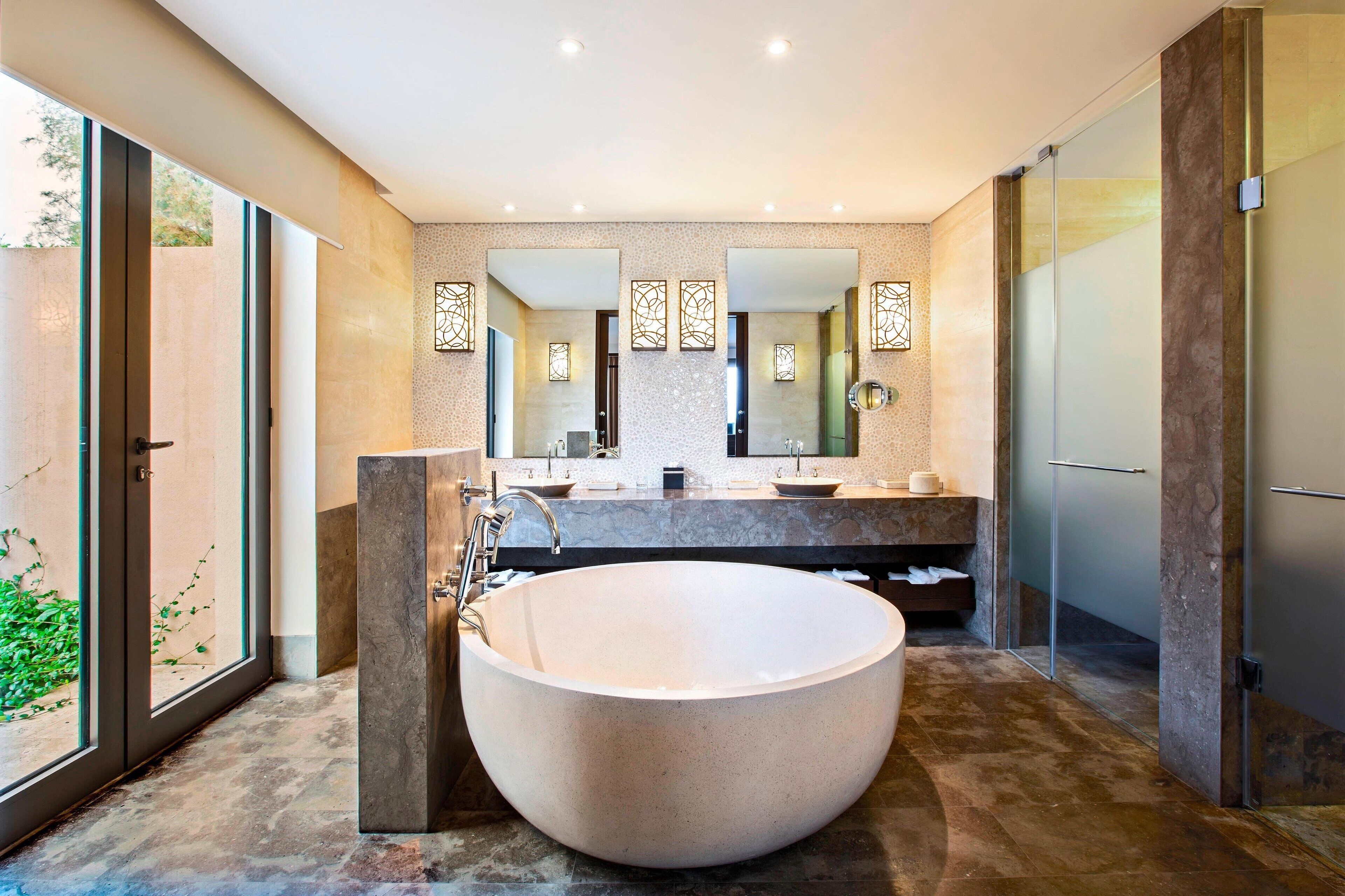 Un baño moderno con una bañera independiente grande, un lavabo doble y un espejo grande sobre el lavabo.