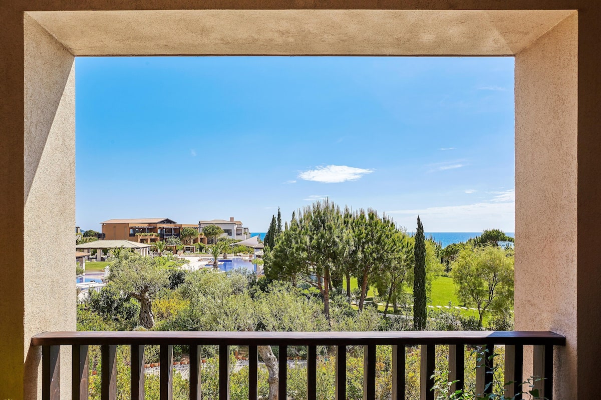 A balcony with a view of a resort area, including a pool and buildings in the background.