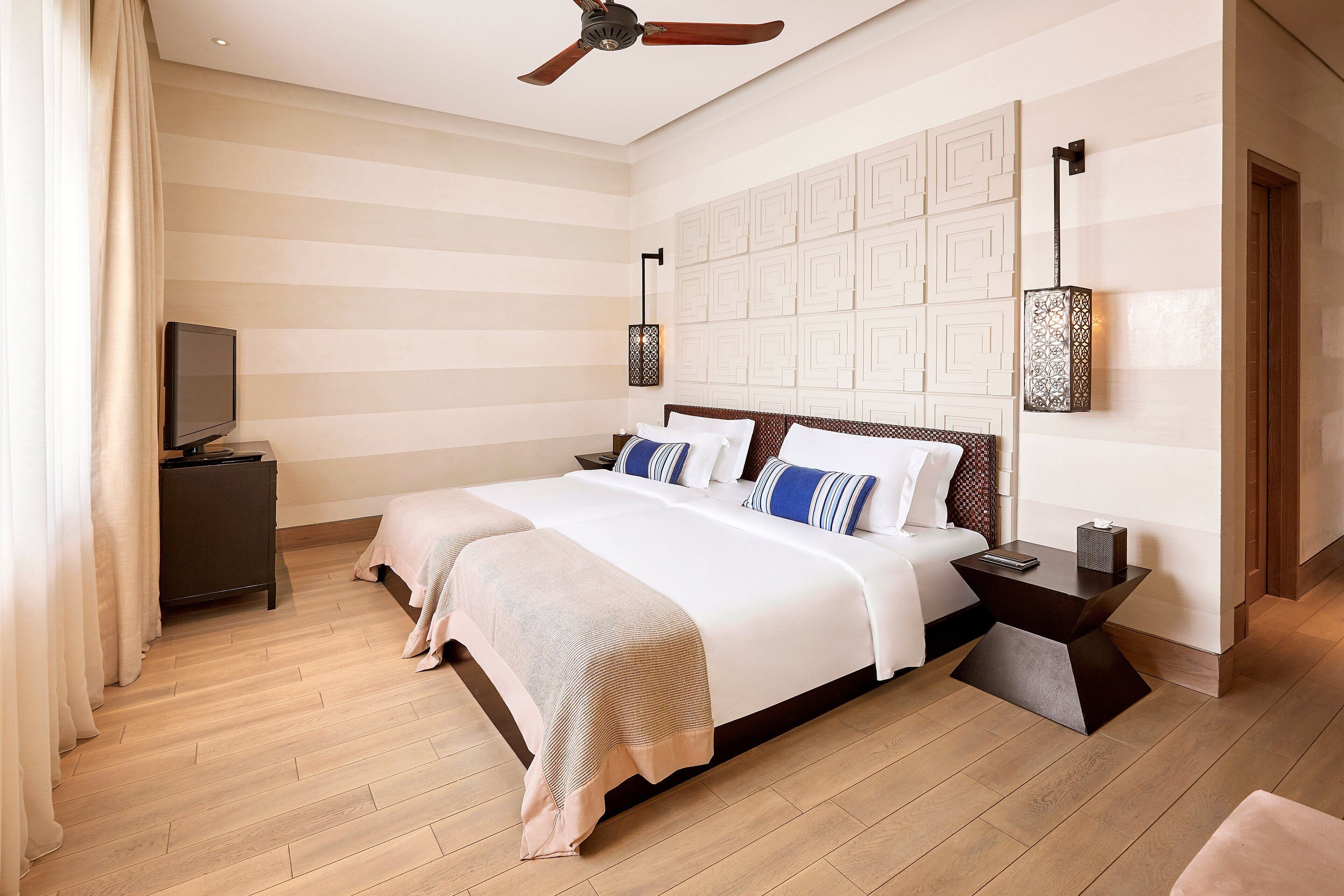 A hotel room with a large bed, a TV, a ceiling fan, and a nightstand.