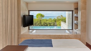 Une chambre d’hôtel moderne dotée d’une grande fenêtre, d’un téléviseur à écran plat, d’une baignoire et d’un lit.
