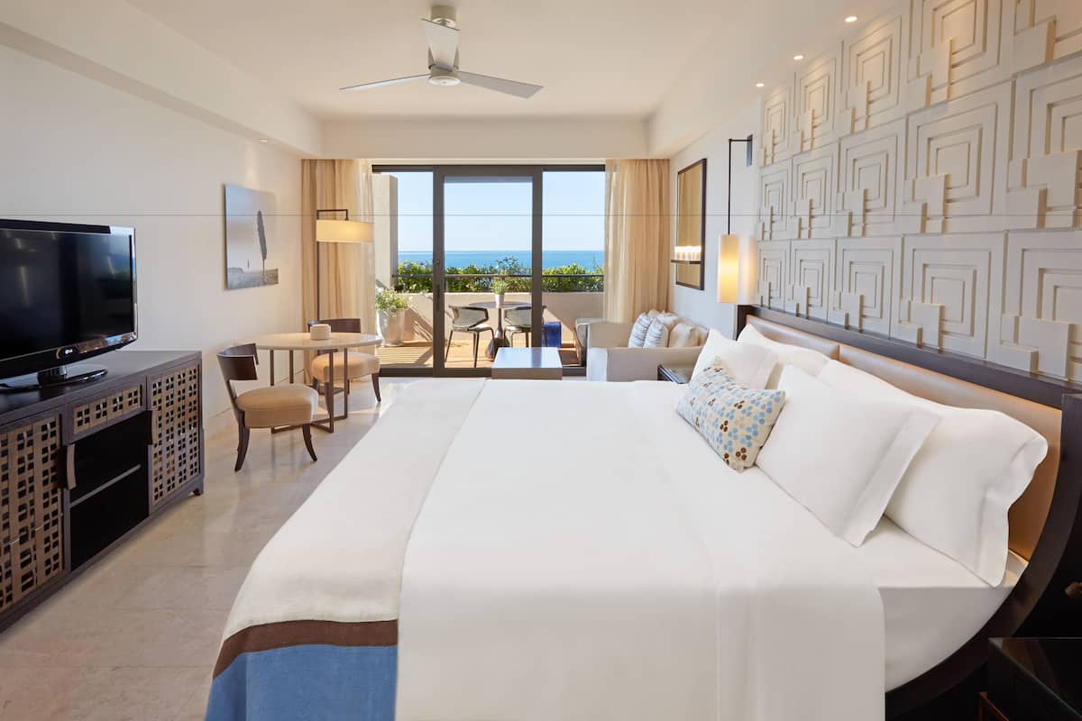 A hotel room with a large bed, a TV, a desk, and a balcony with a view.