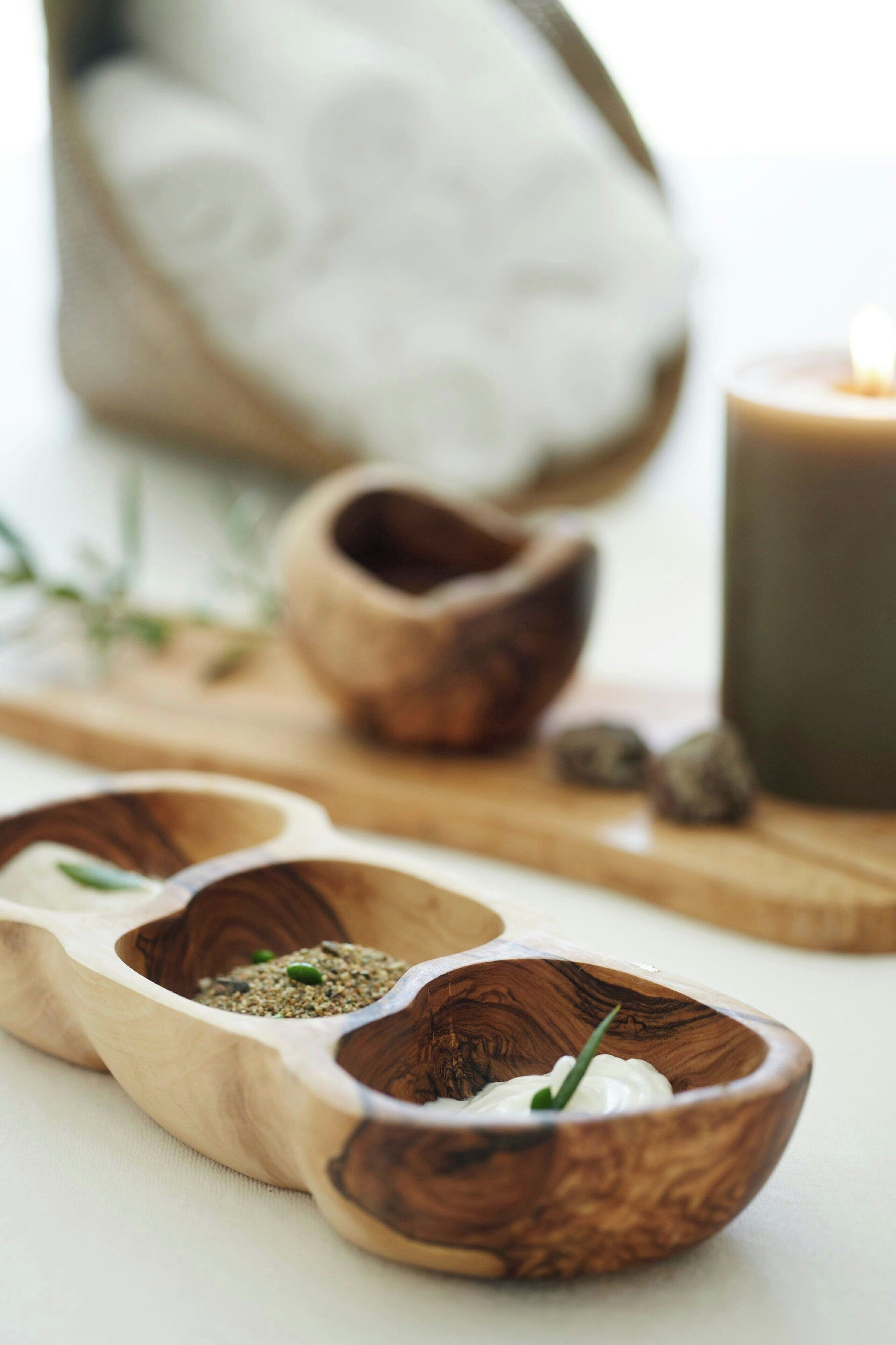 A wooden serving tray with three compartments containing different food items, a candle, and a rustic setting.