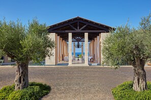 A covered pavilion with a tiled floor, surrounded by trees and a clear blue sky.