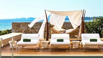 Relax by the pool with a clear view of the sea, surrounded by lounge chairs and a shaded canopy.