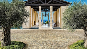 Un espace extérieur abrité, avec un chemin de pierre menant à un bâtiment doté de colonnes et offrant une vue sur la mer.