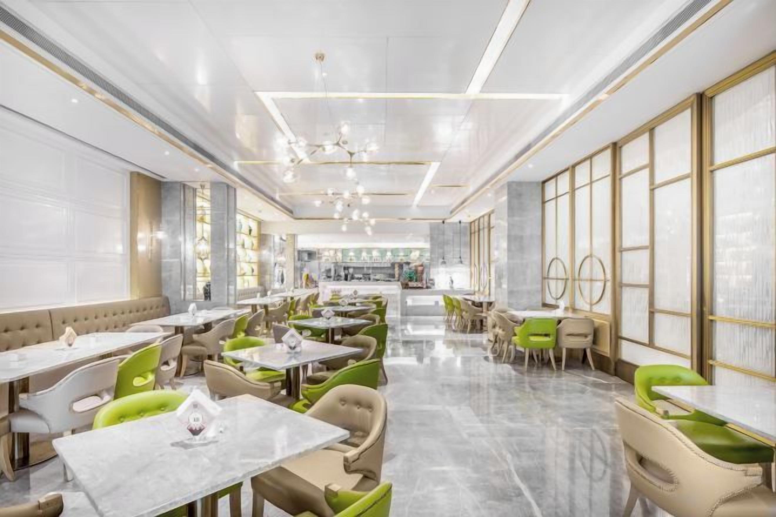 A spacious restaurant with high ceilings, marble flooring, and a mix of green and beige seating.
