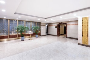 Un hall d’entrée spacieux, doté d’un sol en marbre, de plantes en pot et d’un espace d’accueil avec une porte en bois.