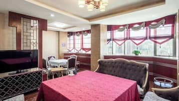 A hotel room with a large bed, a dining table, a TV, and a window with curtains.